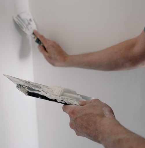 Plasterer finishing an internal wall corner with a broad knife and a trowel loaded with plaster